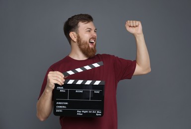 Making movie. Happy man with clapperboard on grey background