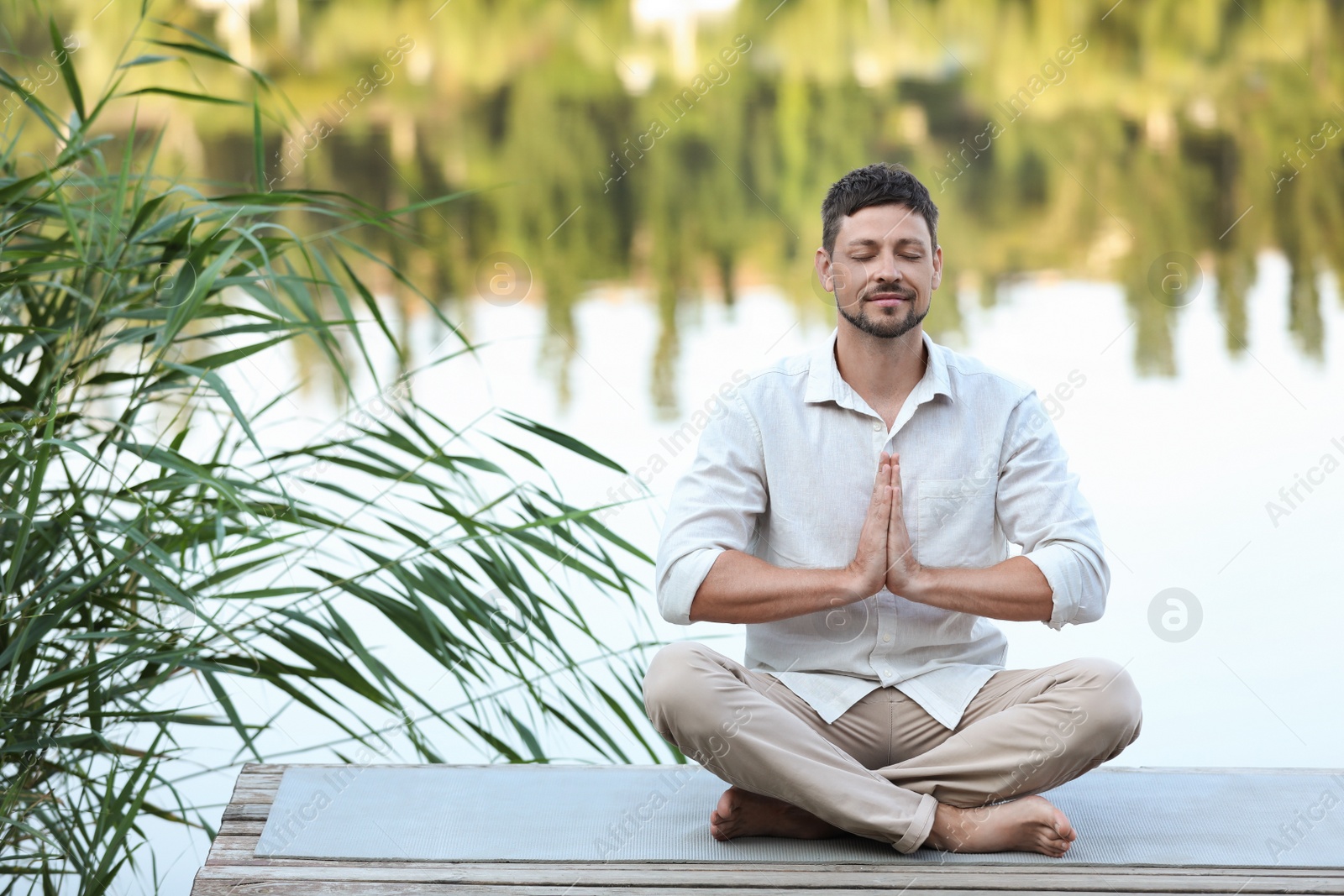 Photo of Man meditating on wooden pier near river. Space for text