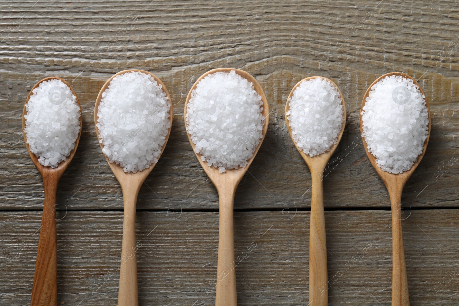 Photo of Organic salt in spoons on wooden table, flat lay