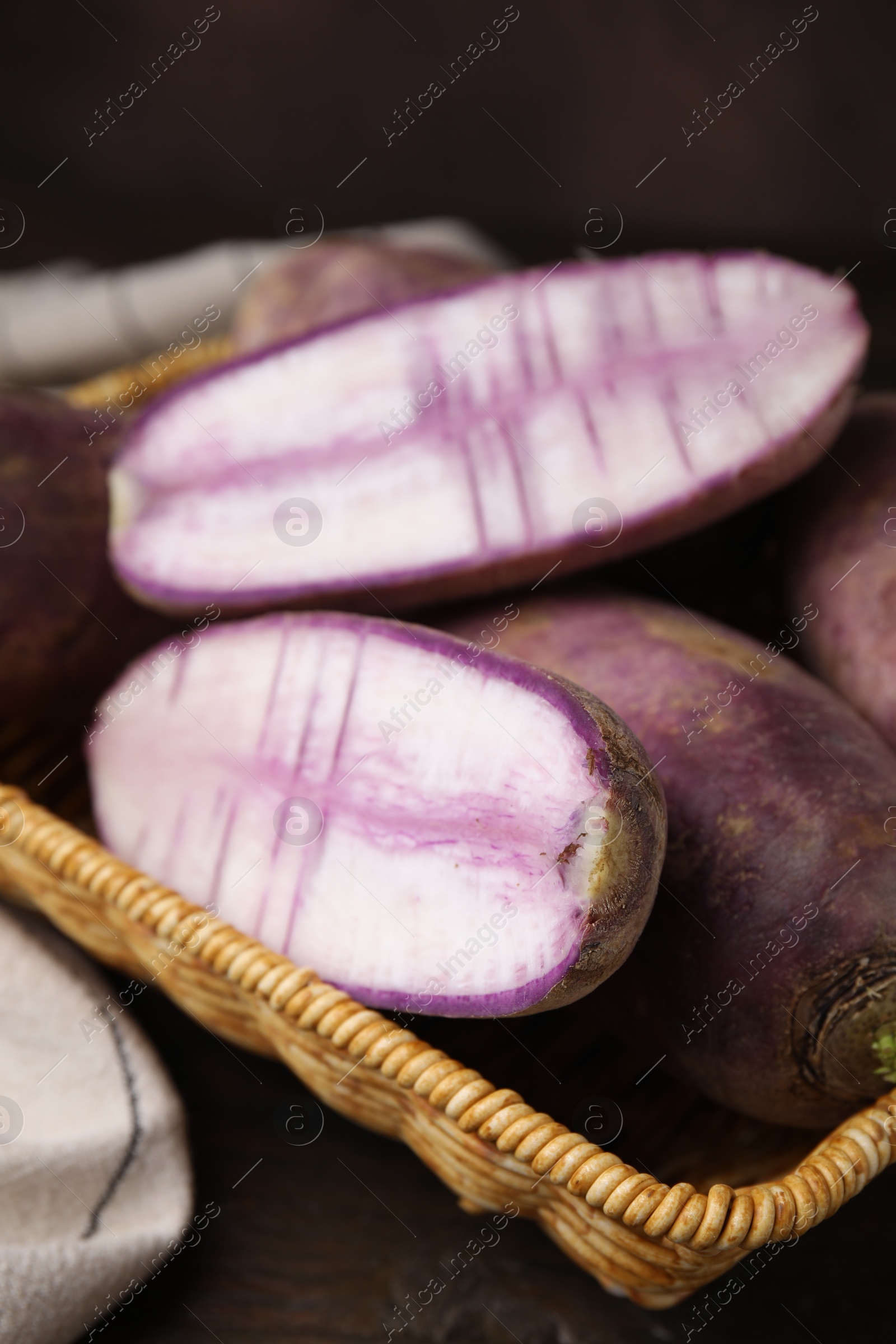 Photo of Purple daikon radishes in wicker basket on wooden table, closeup