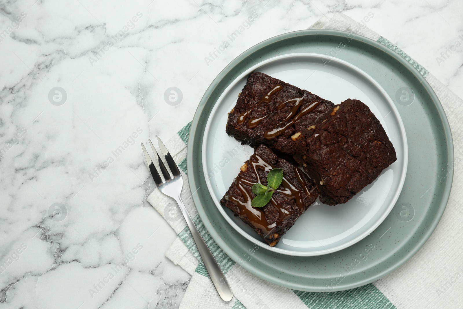 Photo of Delicious chocolate brownies, caramel sauce with nuts and fresh mint on white marble table, top view. Space for text