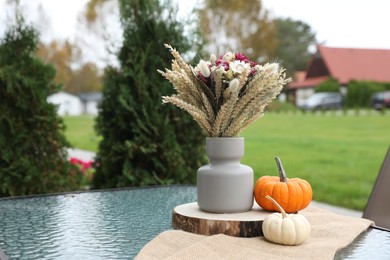 Beautiful bouquet of dry flowers and small pumpkins on glass table outdoors, space for text
