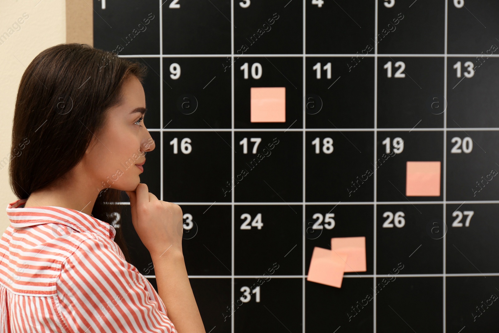 Photo of Young beautiful woman near board calendar  indoors