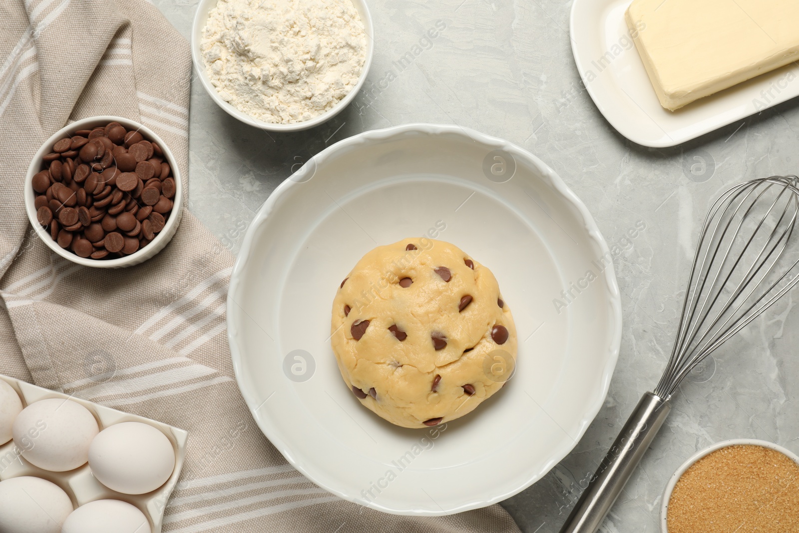 Photo of Fresh dough and different ingredients for cooking chocolate chip cookies on light grey marble table, flat lay