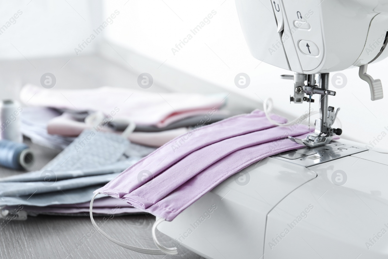 Photo of Sewing machine with homemade protective mask on wooden table, closeup