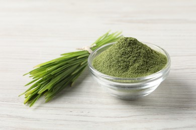 Photo of Wheat grass powder in glass bowl and fresh sprouts on white wooden table, closeup