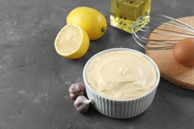 Photo of Fresh mayonnaise sauce in bowl and ingredients on grey table, space for text