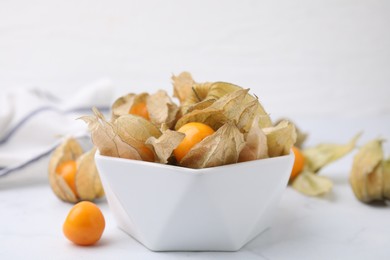 Photo of Ripe physalis fruits with calyxes in bowl on white marble table