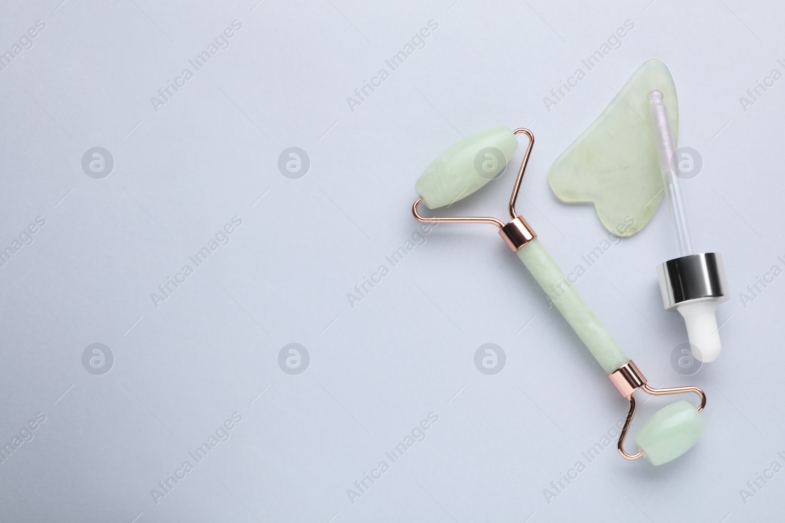 Photo of Gua sha stone, face roller and dropper on light background, flat lay. Space for text