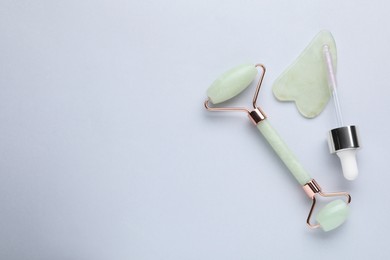 Photo of Gua sha stone, face roller and dropper on light background, flat lay. Space for text