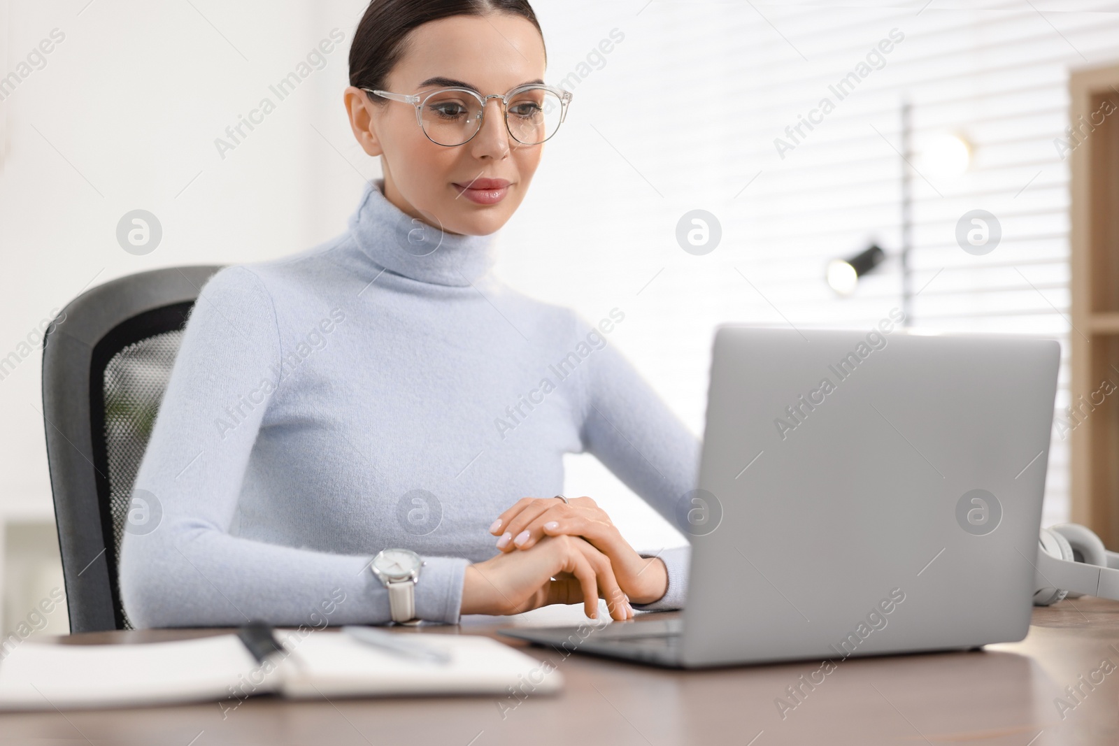 Photo of Young woman in glasses watching webinar at table in office