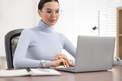 Photo of Young woman in glasses watching webinar at table in office