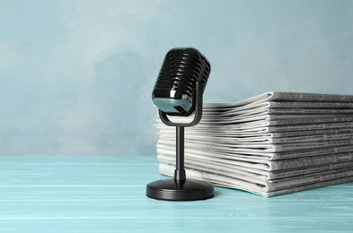 Photo of Newspapers and vintage microphone on light blue wooden table. Journalist's work