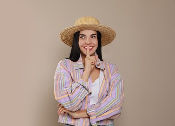 Beautiful young woman with straw hat on beige background