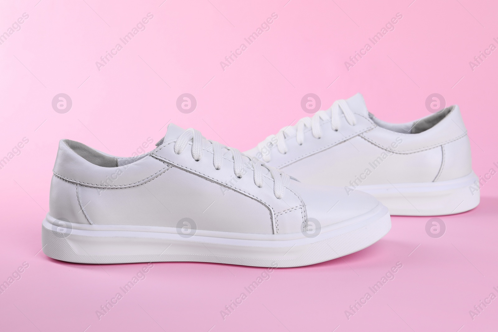 Photo of Pair of stylish white sneakers on pink background