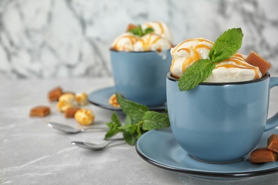 Photo of Delicious ice cream with caramel sauce, candies and mint served on light grey table. Space for text