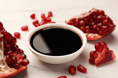 Photo of Bowl of pomegranate sauce and fresh ripe fruit on white marble table, closeup