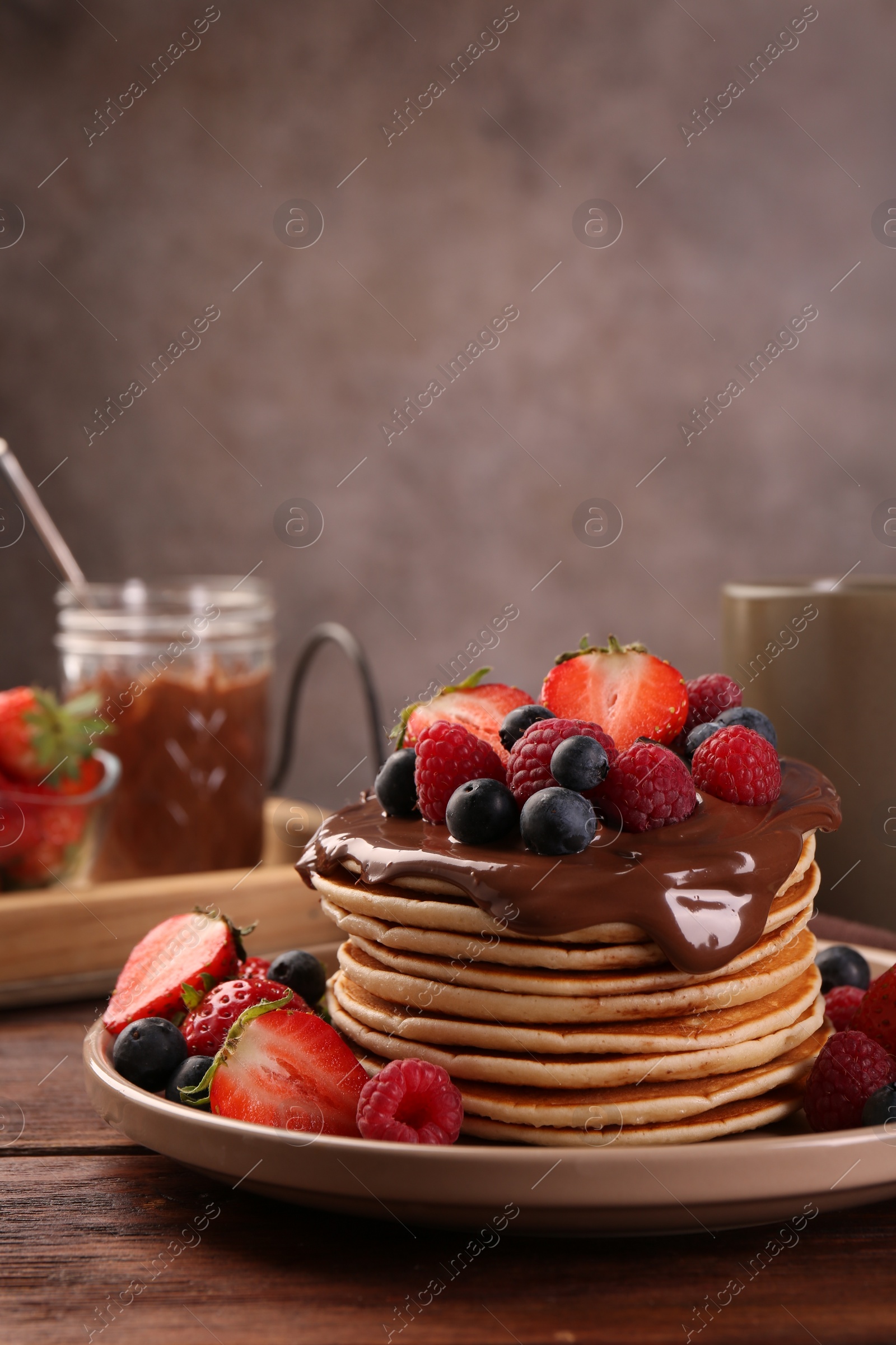 Photo of Stack of tasty pancakes with fresh berries and chocolate spread on wooden table, space for text