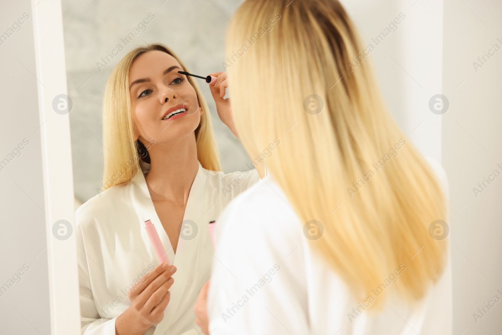 Photo of Beautiful woman applying mascara near mirror in bathroom