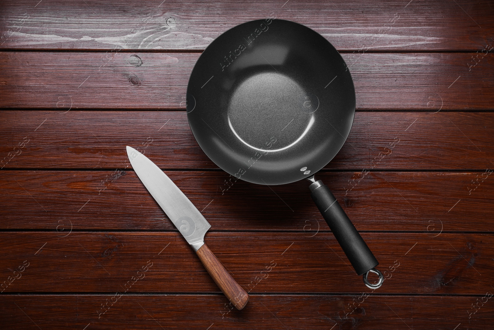 Photo of Empty iron wok and knife on wooden table, flat lay