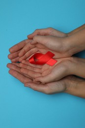 Photo of Woman and girl holding red ribbon on blue background, top view. AIDS disease awareness