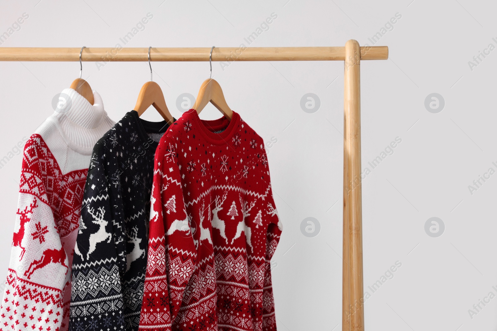 Photo of Different Christmas sweaters hanging on rack against light background