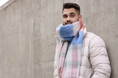 Photo of Smiling man in warm scarf near wall outdoors. Space for text