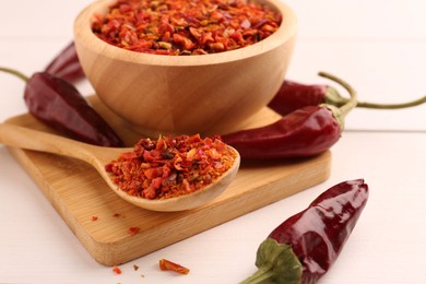 Chili pepper flakes and pods on white wooden table, closeup