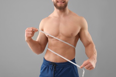 Photo of Happy athletic man measuring waist with tape on grey background, closeup. Weight loss concept