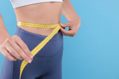 Photo of Slim woman measuring waist with tape on light blue background, closeup and space for text. Weight loss