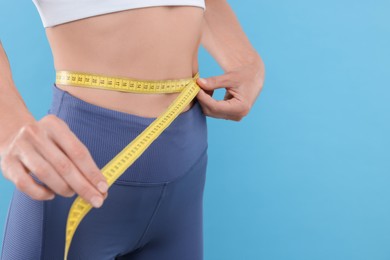 Slim woman measuring waist with tape on light blue background, closeup and space for text. Weight loss