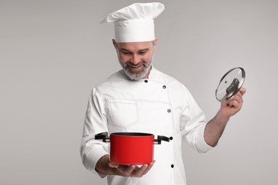 Photo of Happy chef in uniform with cooking pot on grey background