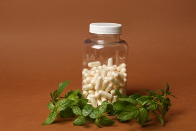 Photo of Transparent medicine bottle and green leaves on brown background
