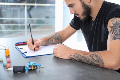 Professional tattoo artist drawing sketch at table indoors