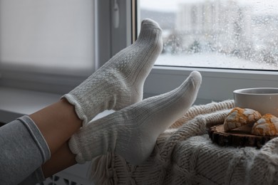 Woman in knitted socks relaxing near window at home, closeup