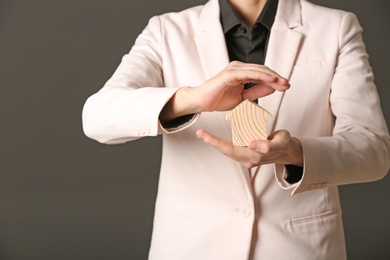 Photo of Female agent holding wooden house on dark background, closeup. Home insurance