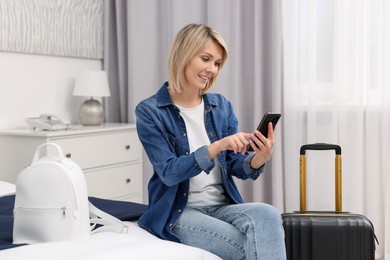 Photo of Smiling guest with smartphone relaxing on bed in stylish hotel room