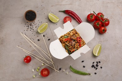 Photo of Box of wok noodles with vegetables and meat on light table, flat lay