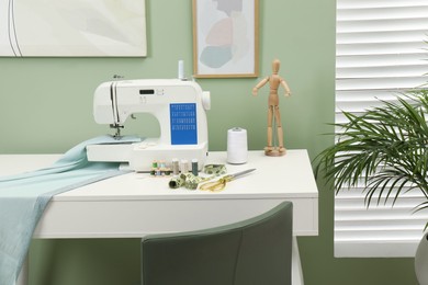 Photo of Modern sewing machine with cloth and craft accessories on white table near window in room