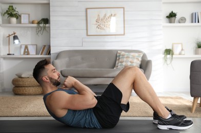 Handsome man doing abs exercise on yoga mat at home