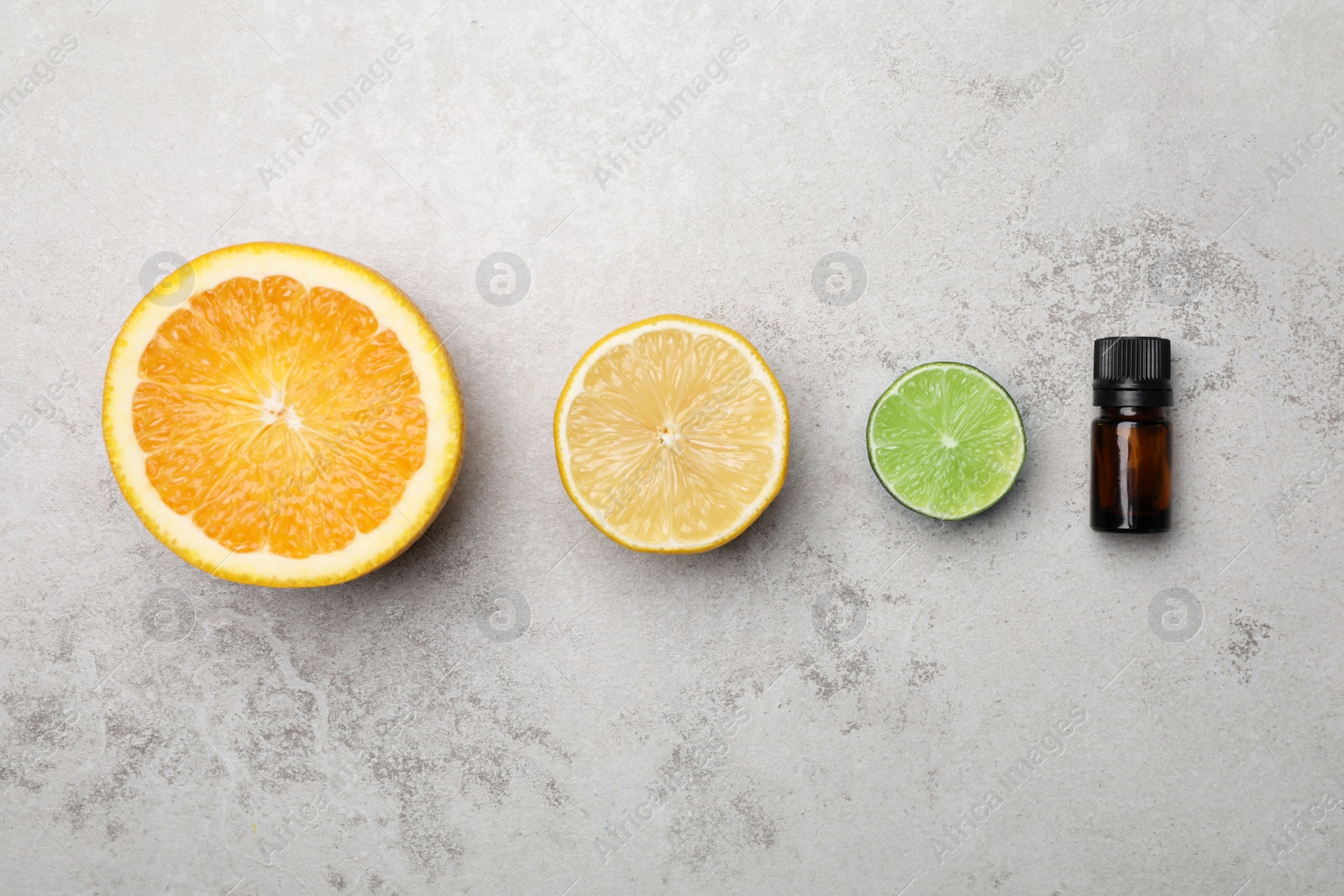 Photo of Bottle of citrus essential oil and fresh fruits on light table, flat lay