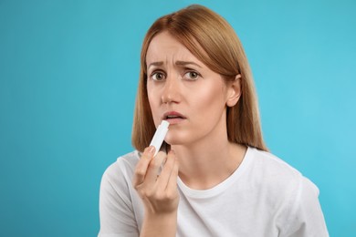 Photo of Upset woman with herpes applying lip balm against light blue background
