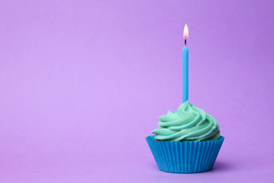 Photo of Delicious birthday cupcake with turquoise cream and burning candle on violet background. Space for text