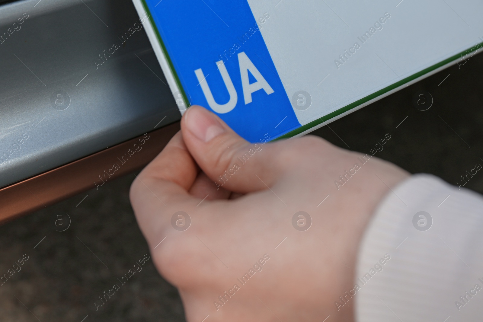 Photo of Woman installing vehicle registration plate outdoors, closeup