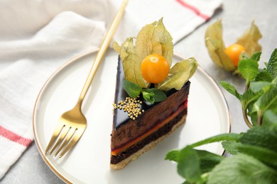 Piece of tasty cake decorated with physalis fruit on light grey table