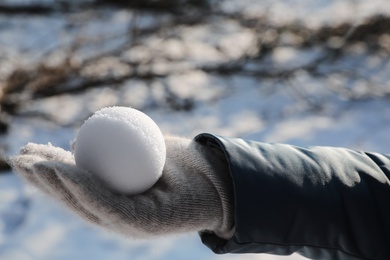 Woman holding snowball outdoors on winter day, closeup. Space for text