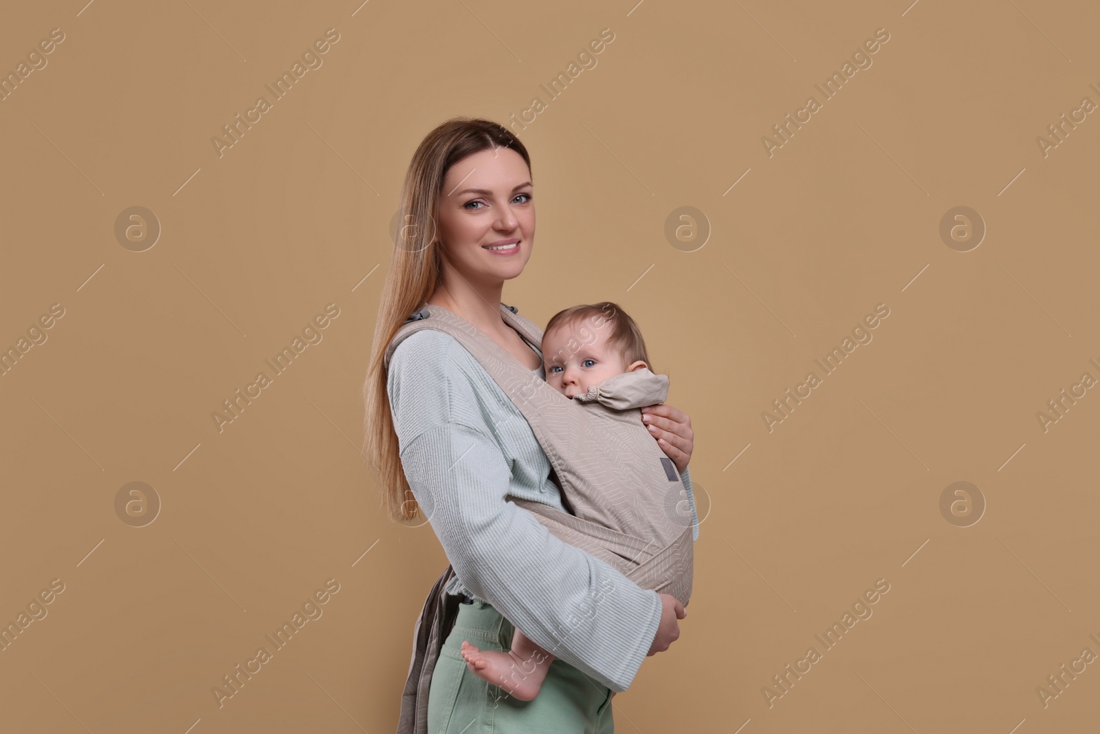 Photo of Mother holding her child in sling (baby carrier) on light brown background