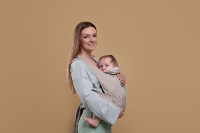 Mother holding her child in sling (baby carrier) on light brown background