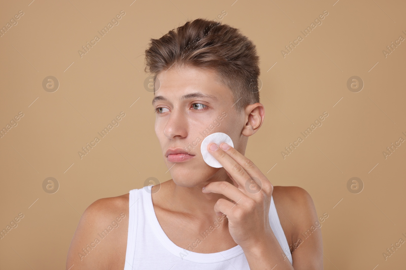 Photo of Handsome man cleaning face with cotton pad on beige background