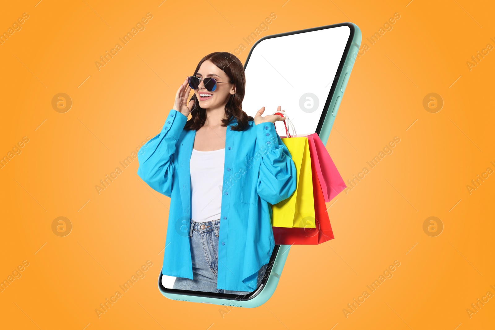 Image of Online shopping. Happy woman with paper bags looking out from smartphone on orange background